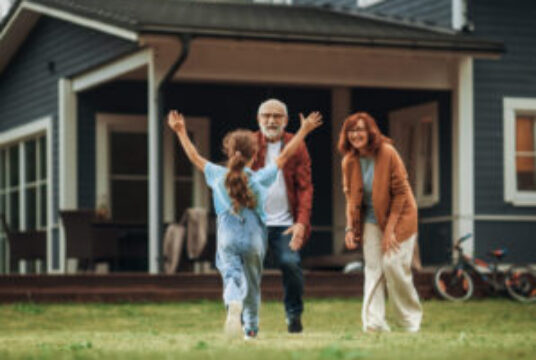 Older couple in front of their house greeting a granddaughter who is approaching with arms open for a hug. Estate planning concept.
